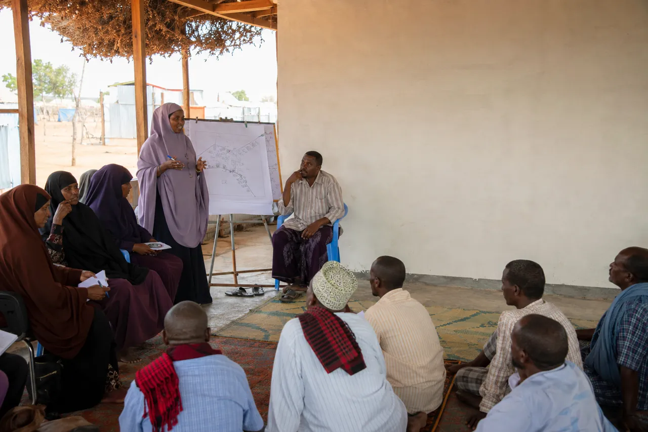 Somali women and men participating in a community consultation, reviewing a site map together.